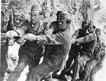 a number of men in SS uniforms and wearing fez headgear straining to pull on a rope.