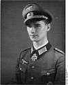 A man wearing a peaked cap and military uniform with an Iron Cross displayed at the front of his uniform collar.