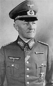 A man wearing a peaked cap, military uniform with an Iron Cross displayed at the front of his uniform collar.