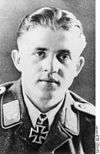 A man wearing a military uniform with an Iron Cross displayed at his neck.