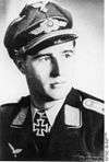 A man wearing a peaked cap, military uniform with an Iron Cross displayed at the front of his uniform collar.