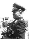 A man in semi profile wearing a peaked cap and military uniform with various military decorations.