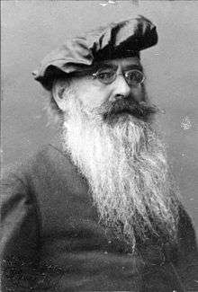 An elderly, bearded white man. He wears glasses and a beret.