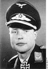 A man wearing a military uniform, peaked cap, and an Iron Cross displayed at the front of his uniform collar.