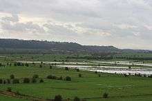 Water on grassy lowland with hills in the distance.