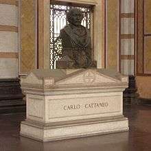 A white marble sarcophagus, surmounted by a bronze bust of the deceased, inside a chapel