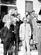 A black and white photograph of about ten white men in three-piece suits standing on the steps of a building with columns