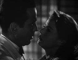 Black-and-white film screenshot of a man and woman as seen from the shoulders up. The two are close to each other as if about to kiss.