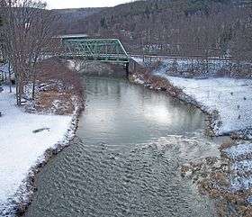 A view of a creek with a truss bridge in the near background and another bridge in the far background.