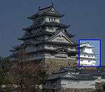 A small three-storied castle tower next to a large five-storied tower. Both have white walls, dark roofs and are built on a platform of unhewn stones.