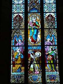 Stained glass windows depicting the Virgin with Jesus in the middle, surrounded by a bishop, an old crowned man on his knees and a crowned young man