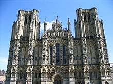 Large ornate grey stone facade of a building. Symmetrical ith towers either side.