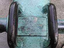 Photograph of the placard affixed to the Cavite cannon located in Village Green Park, Winnetka, Illinois, USA. The placard reads: "THIS GUN WAS MOUNTED ON THE DEFENSES OF CAVITE ARSENAL WHICH WAS SURRENDERED TO COMMODORE GEORGE DEWEY MAY 7 1898."