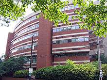 A circular, six-story brick building with decorative white concrete stripes above and below lines of adjacent square windows that encircle most of each level