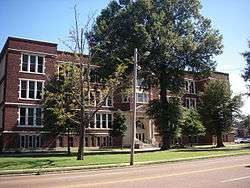 A multi-layered brick building with a tree obscuring the front of it.