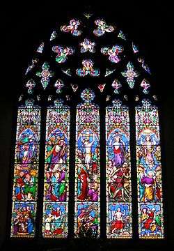 This stained glass window is divided into five long sections, above which the stone tracery looks like a lacey medallion. The colours are not like Medieval glass; there is a lot of bright red, pale blue, apple green, mauve and pink.