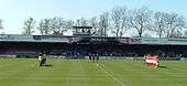 One of the stands of the Bootham Crescent association football ground, with supporters sitting down and players standing on a grass field below