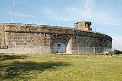 View of the front exterior of the fort showing an arc of casemates, with a structure on the roof