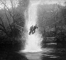 Two men crossing a rope bridge over water