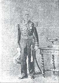 Tintype photograph depicting a full-length portrait of an elderly, bearded man wearing an elaborately embroidered military dress uniform with sword and holding an embroidered and plumed bicorn hat in his right hand