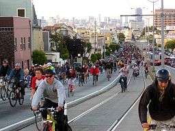 Many cyclists on a road, all going in the same direction.