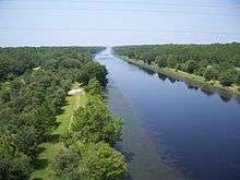 View down on a canal approximately 100 feet across disappearing into the horizon, bordered by trees