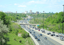 A six-lane highway descends into a forested valley, ascending out of the valley in the distance.