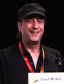 A man wearing a cap smiles as he looks into the distance.