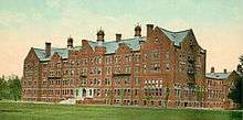 A long five-story brown brick building stands before a broad green lawn.