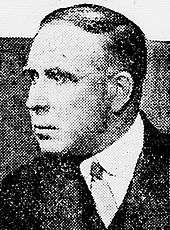 Black and white portrait photo of a white man wearing a jacket and tie