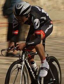 A cyclist in the Cervélo jersey wearing a skinsuit and an aerodynamic white helmet. He is crouched low over his bicycle.