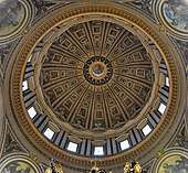  Photo looking up at the dome's interior from below. The dome is decorated at the top with a band of script. Around its base are windows through which the light streams. The decoration is divided by many vertical ribs which are ornamented with golden stars.