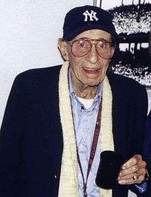 Eddie Layton wearing a New York Yankees cap and holding a mug