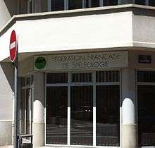 Windows of a modern-fronted office building on a city street, with a sign above which reads "Fédération française de spéléologie".