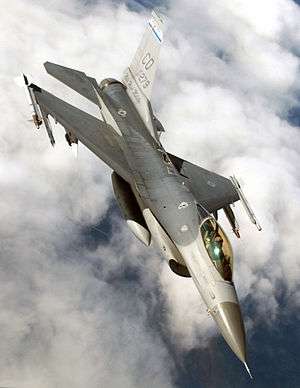 Upright aerial photo of gray jet aircraft flying above clouds.