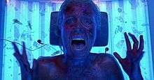 An image of Ashley, a blonde woman, looking directly at the camera and screaming inside a tanning bed.