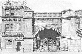 Three-story office building next to a railway arch, with an ornate gate in front of it.