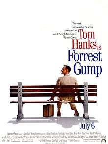 Film poster with an all-white background and a park bench (facing away from the viewer) near the bottom. A man wearing a white suit is sitting on the right side of the bench and is looking to his left while resting his hands on both sides of him on the bench. A suitcase is sitting on the ground, and the man is wearing tennis shoes. At the top left of the image is the film's tagline and title and at the bottom is the release date and production credits.