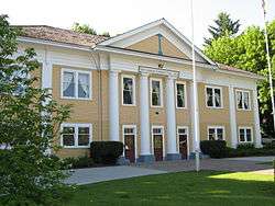 A yellow two-story building with a freshly-mowed lawn and two flagpoles.