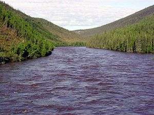 A choppy river is seen surrounded by tree-covered hills.