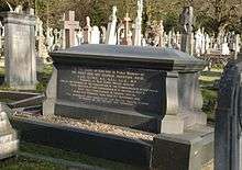 A black polished funerary monument with gold inscriptions, surrounded by many other graves