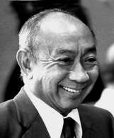 Black and white photograph of the head and shoulders of a balding Chinese man in a suit and tie, smiling broadly