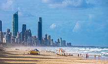 A beach populated by people; a city can be seen in the horizon