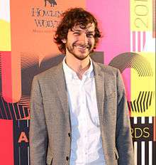 A man wearing a grey suit smiling for cameras.