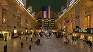 People walk through a large symmetrical room as an American flag hangs vertically at the center of the far wall.