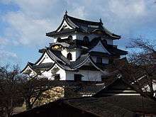 A castle with white walls, dark roofs and many gables on a platform of unhewn stones.