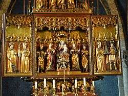 The central section of an elaborately carved, painted and gilded altarpiece showing the Virgin Mary and Christ Child seated in majesty and surrounded by saints and angels. Although the flesh and some details are painted in colour, most of the surfaces are gilt. The figures are all chubby-faced and have a charming quality.