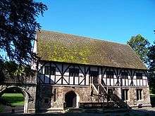 Two story building with half timber second floor built over the stone first floor. Wooden staircase goes to the entrance on the second floor.