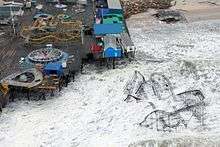 A roller coaster sitting in the ocean; a damaged pier