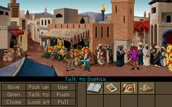 A video game screenshot showing the two protagonists in the middle of a crowded marketplace. The lower part of the image shows a variety of objects on the right side and a number of verbs such as "Pick up", "Use" and "Talk to" on the left side. The mouse cursor is pointing at Sophia, making the current command "Talk to Sophia".